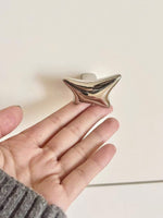 Hand holding a polished chrome wave star knob showing sculptural curved finish