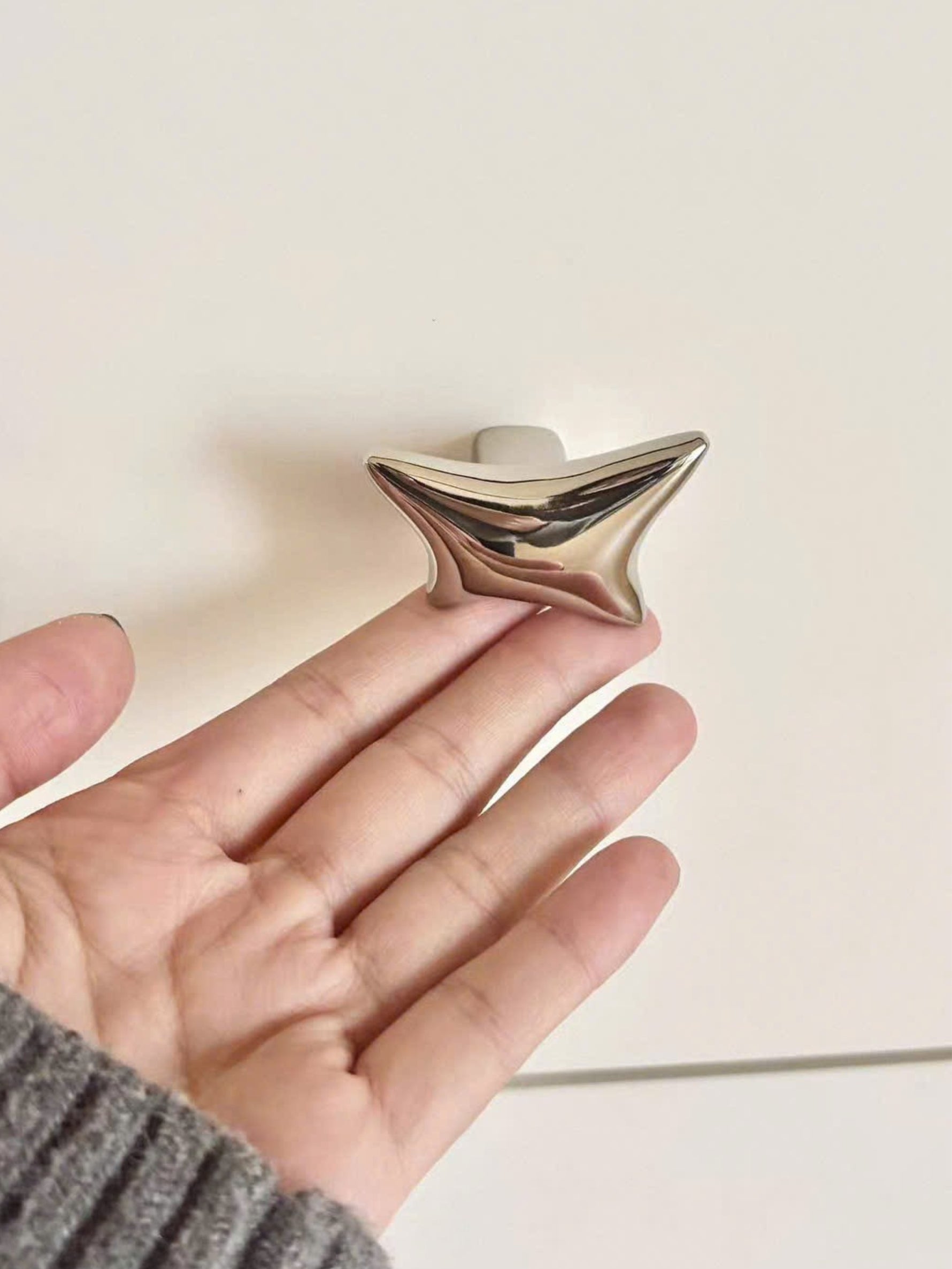 Hand holding a polished chrome wave star knob showing sculptural curved finish