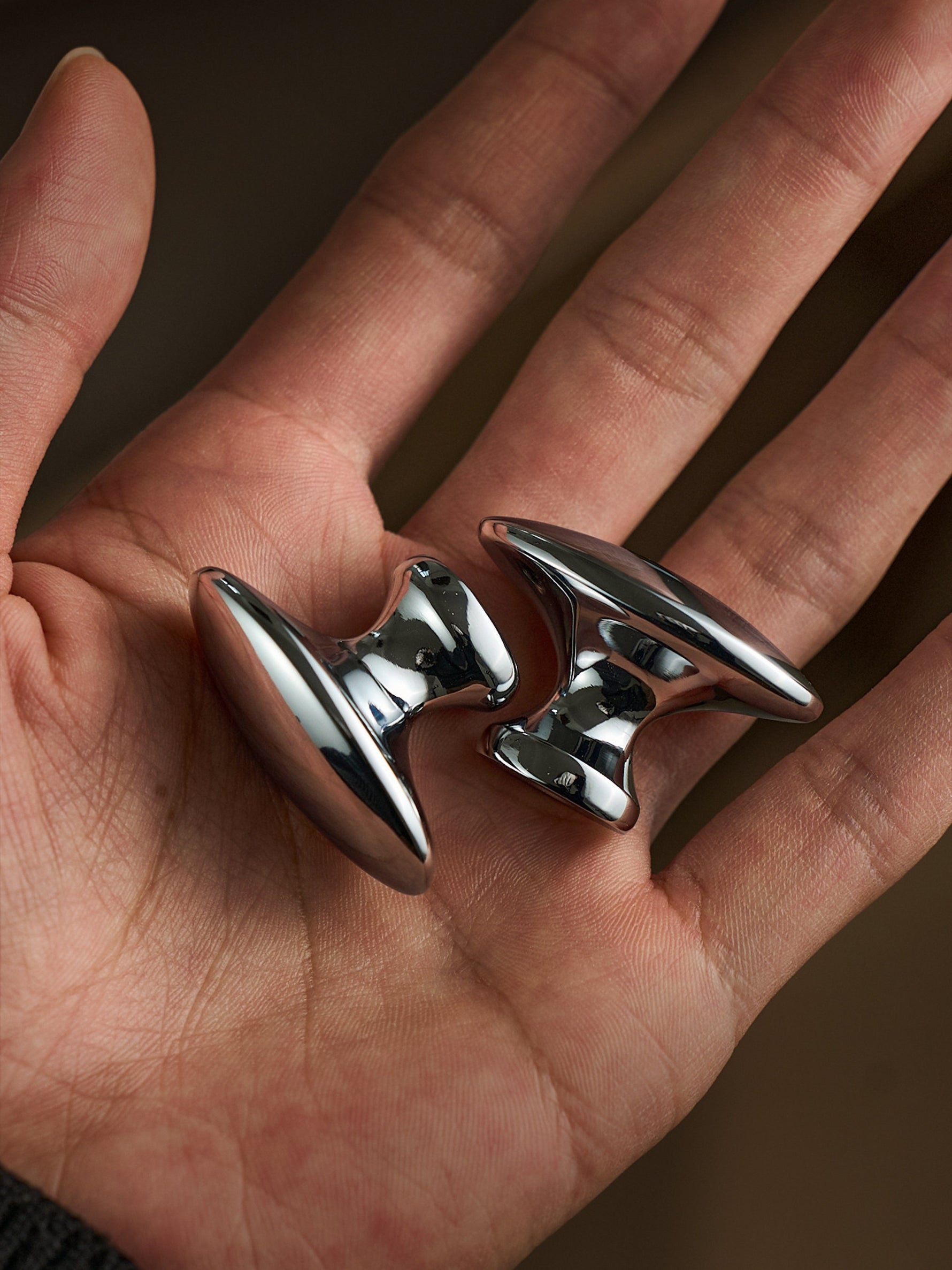 Two polished chrome oval cabinet knobs held in open palm, macro view