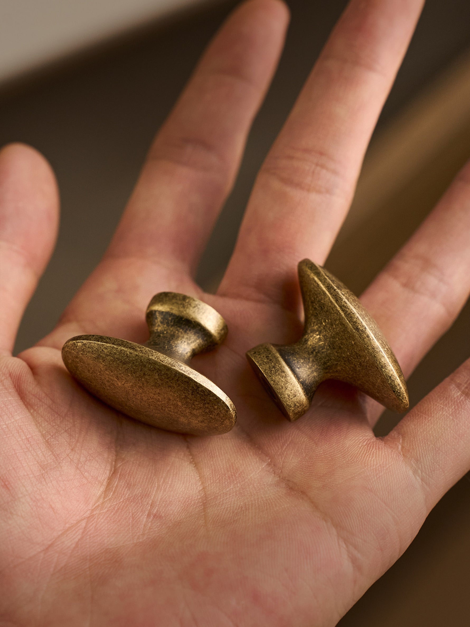 Two antique brass oval cabinet knobs held in open palm, macro view