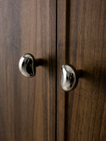 Two polished chrome pebble knobs on dark walnut wood cabinet doors, close-up
