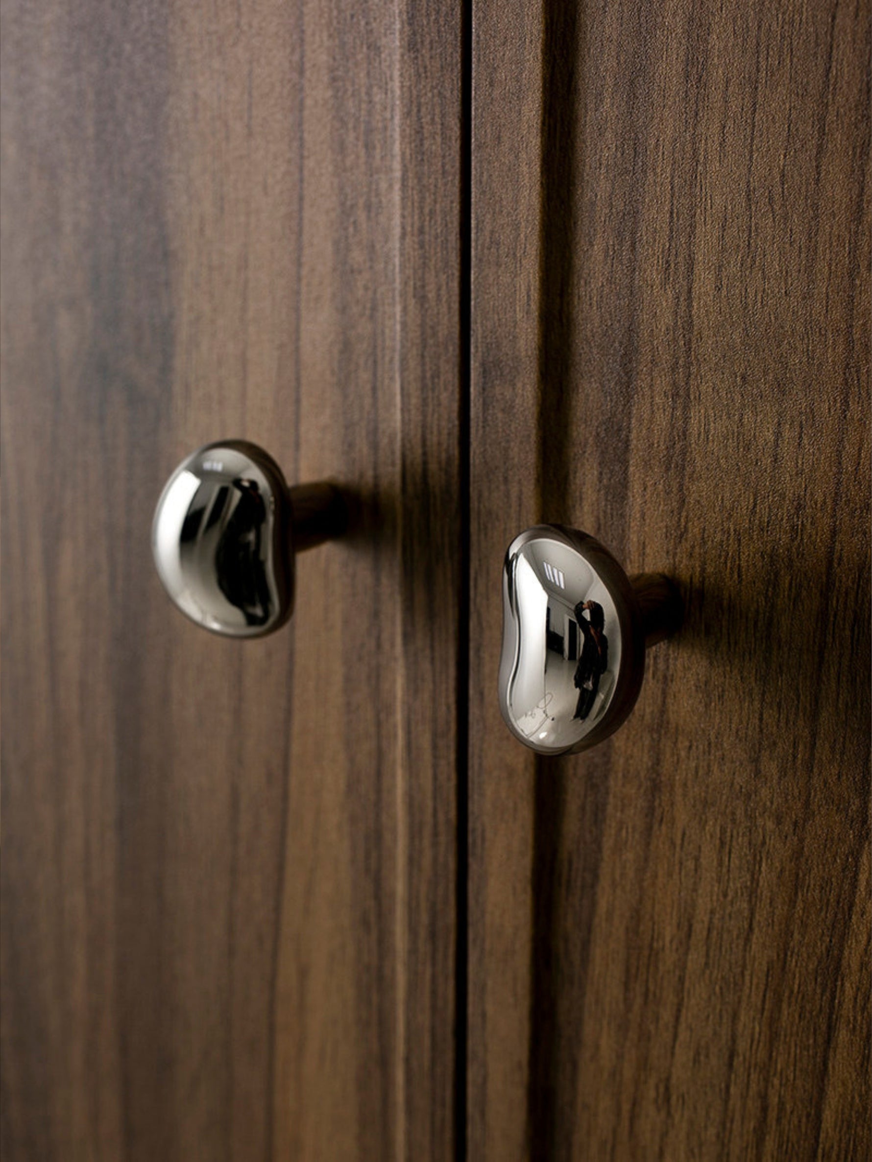 Two polished chrome pebble knobs on dark walnut wood cabinet doors, close-up
