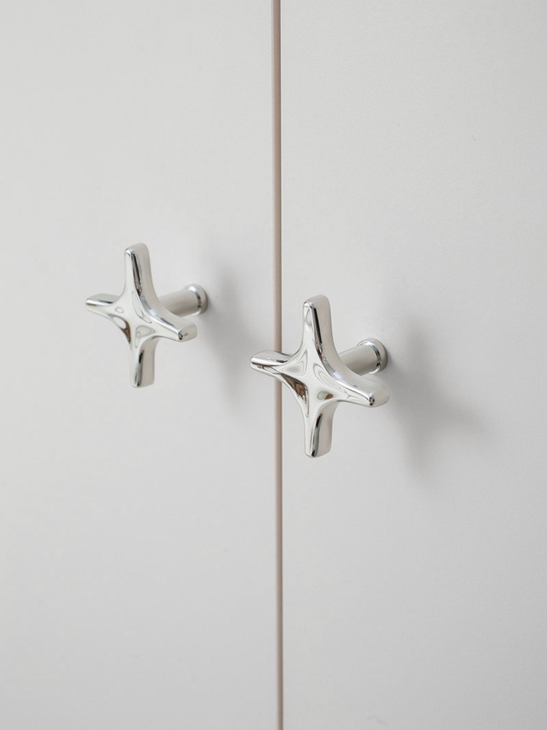 Two polished chrome star knobs on white cabinet doors with visible mounting posts