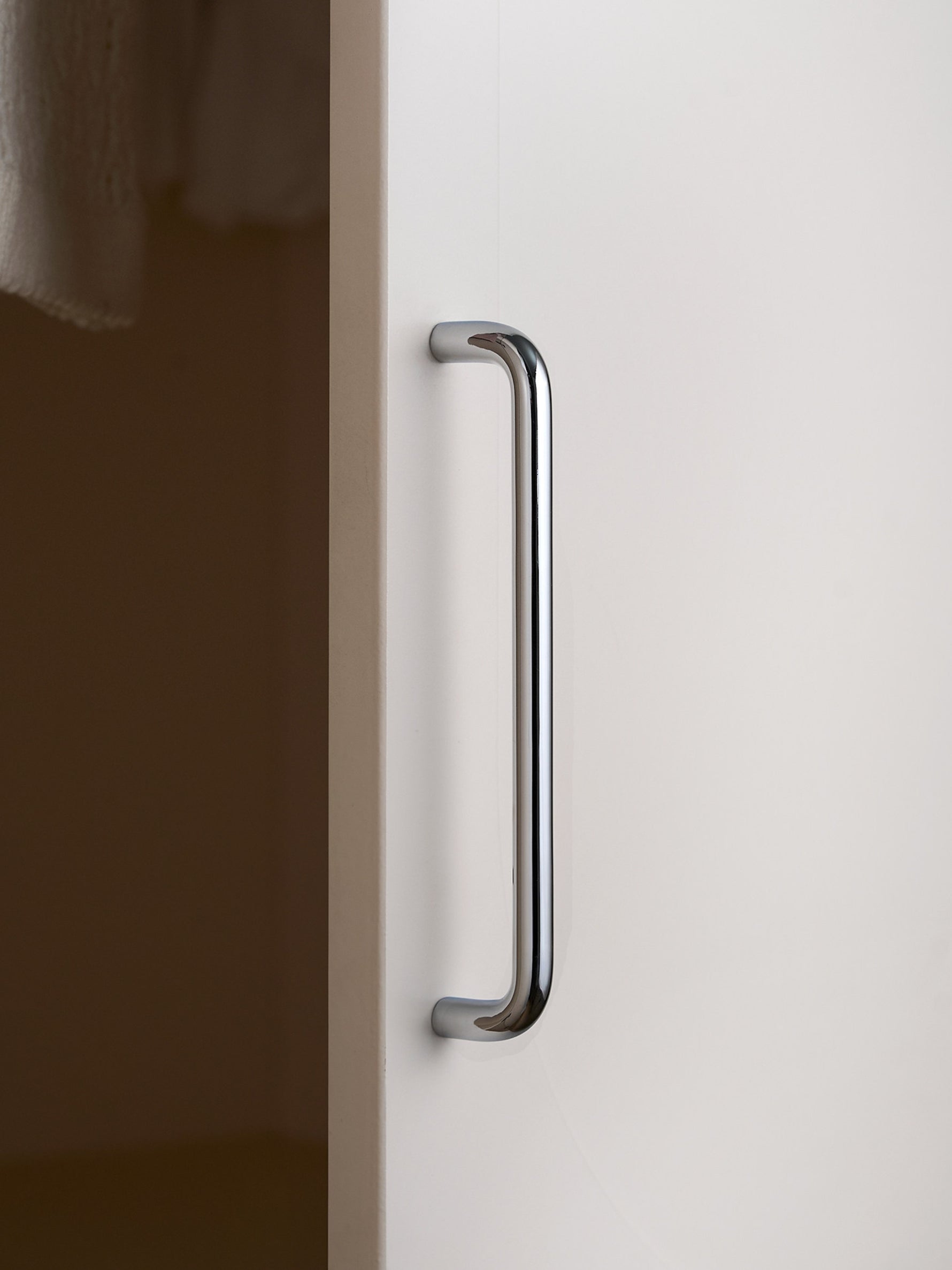 Single polished chrome bar pull on white wardrobe door, side view