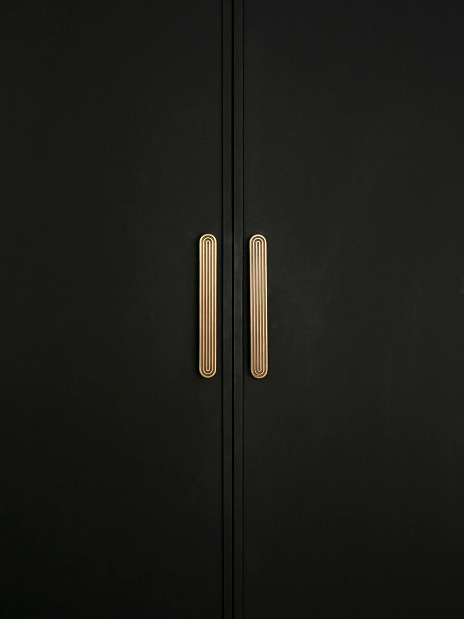 Close-up pair of solid brass Art Deco arch pulls on matte black wardrobe doors