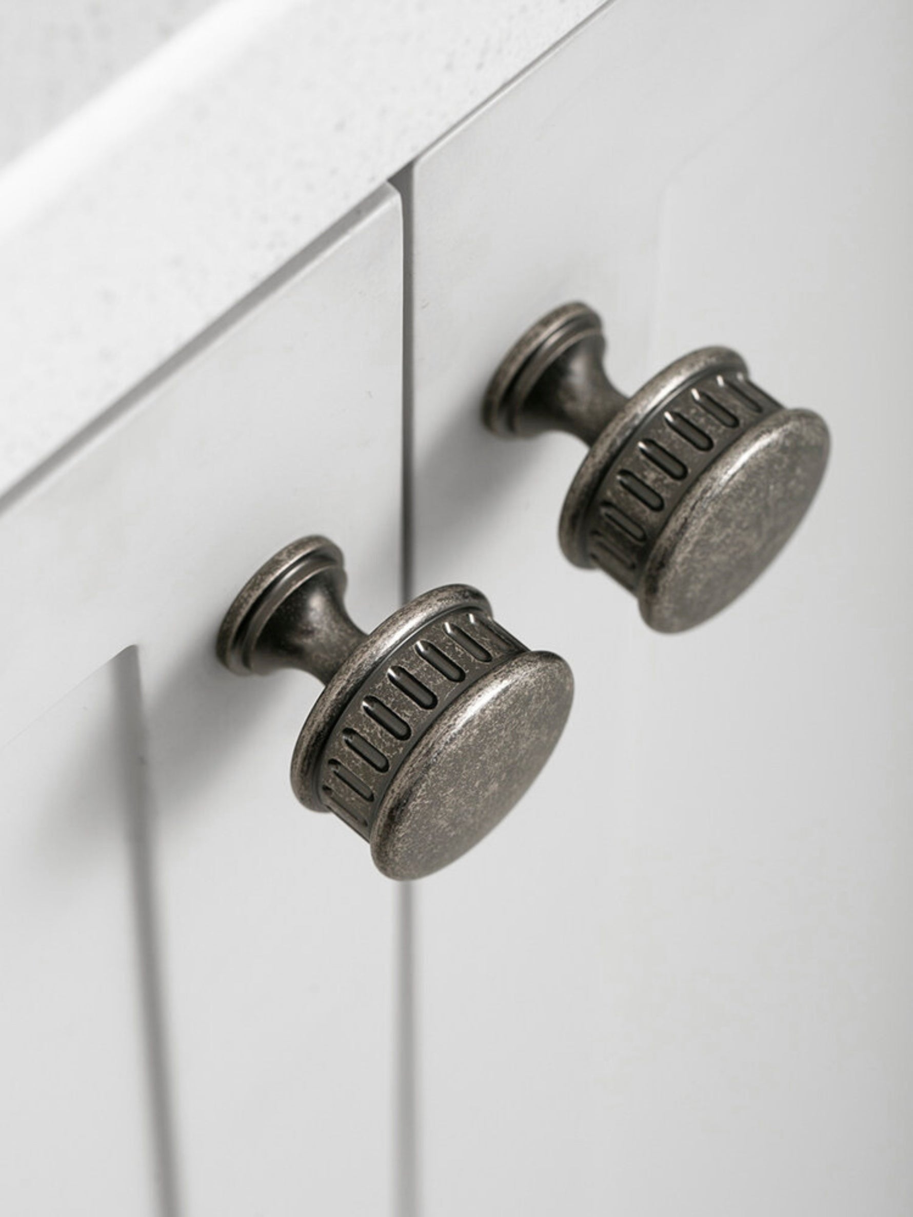 Two antique silver reeded cabinet knobs on white kitchen cabinet, close-up