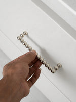 Hand holding a polished chrome beaded ball pull against white cabinet door