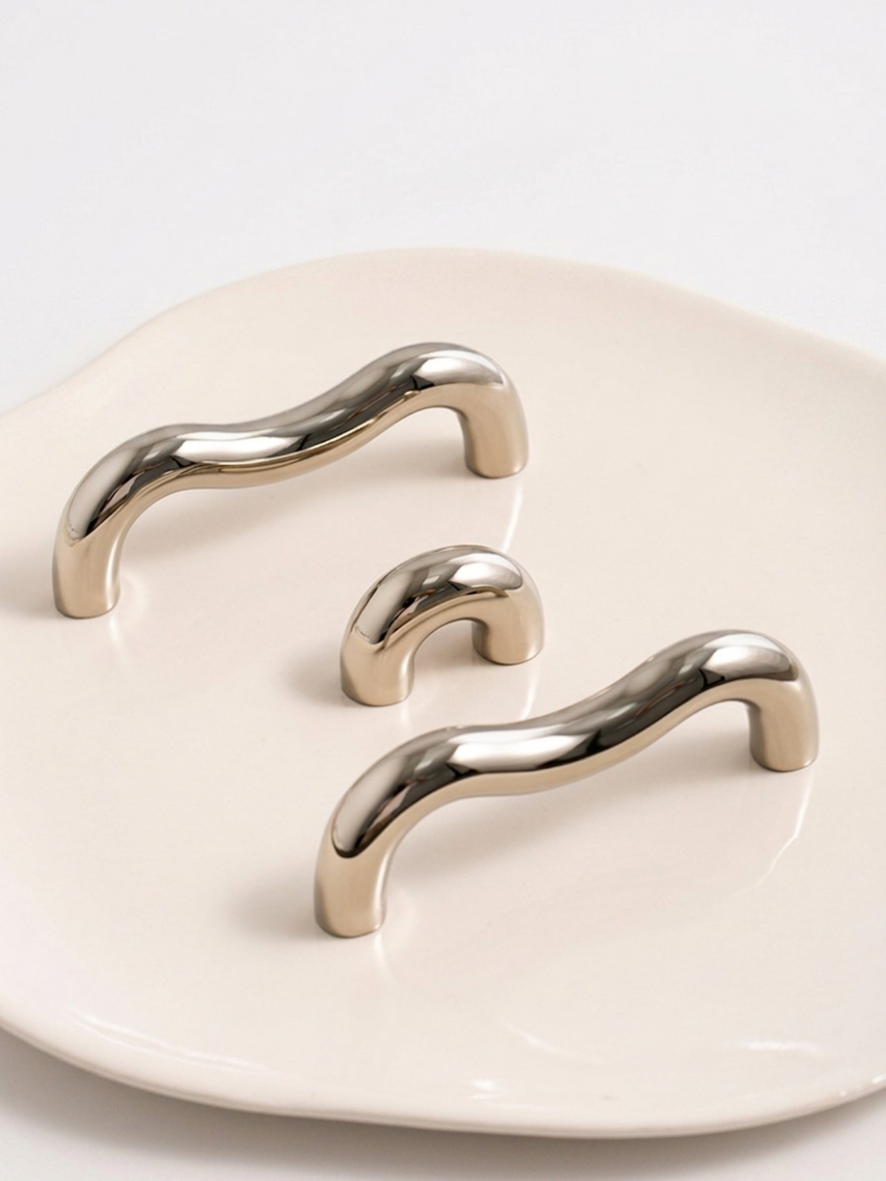 Three nickel chrome wavy pulls and arch knobs on cream ceramic tray