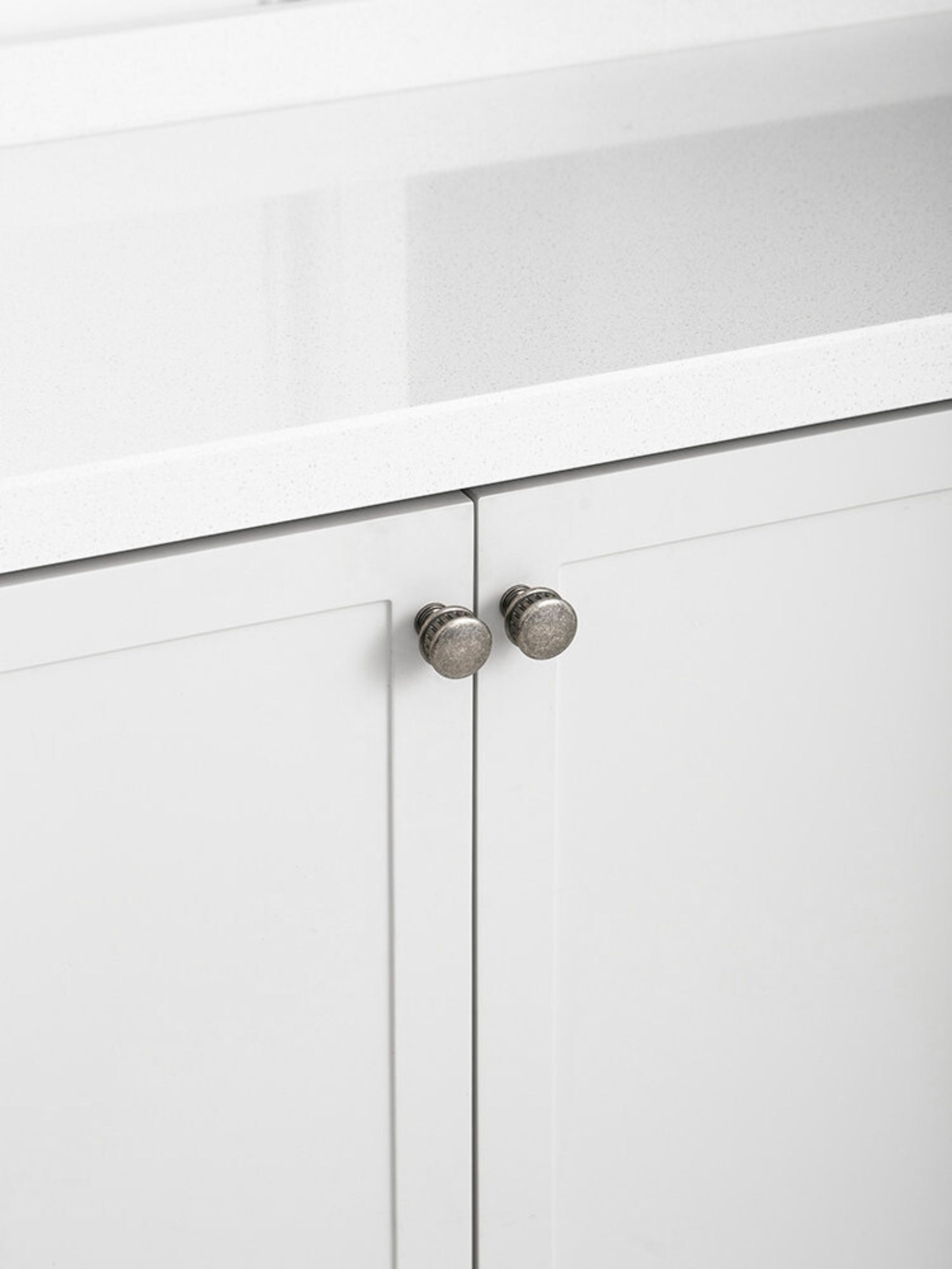 Two antique silver knobs on white shaker kitchen cabinet under stone countertop