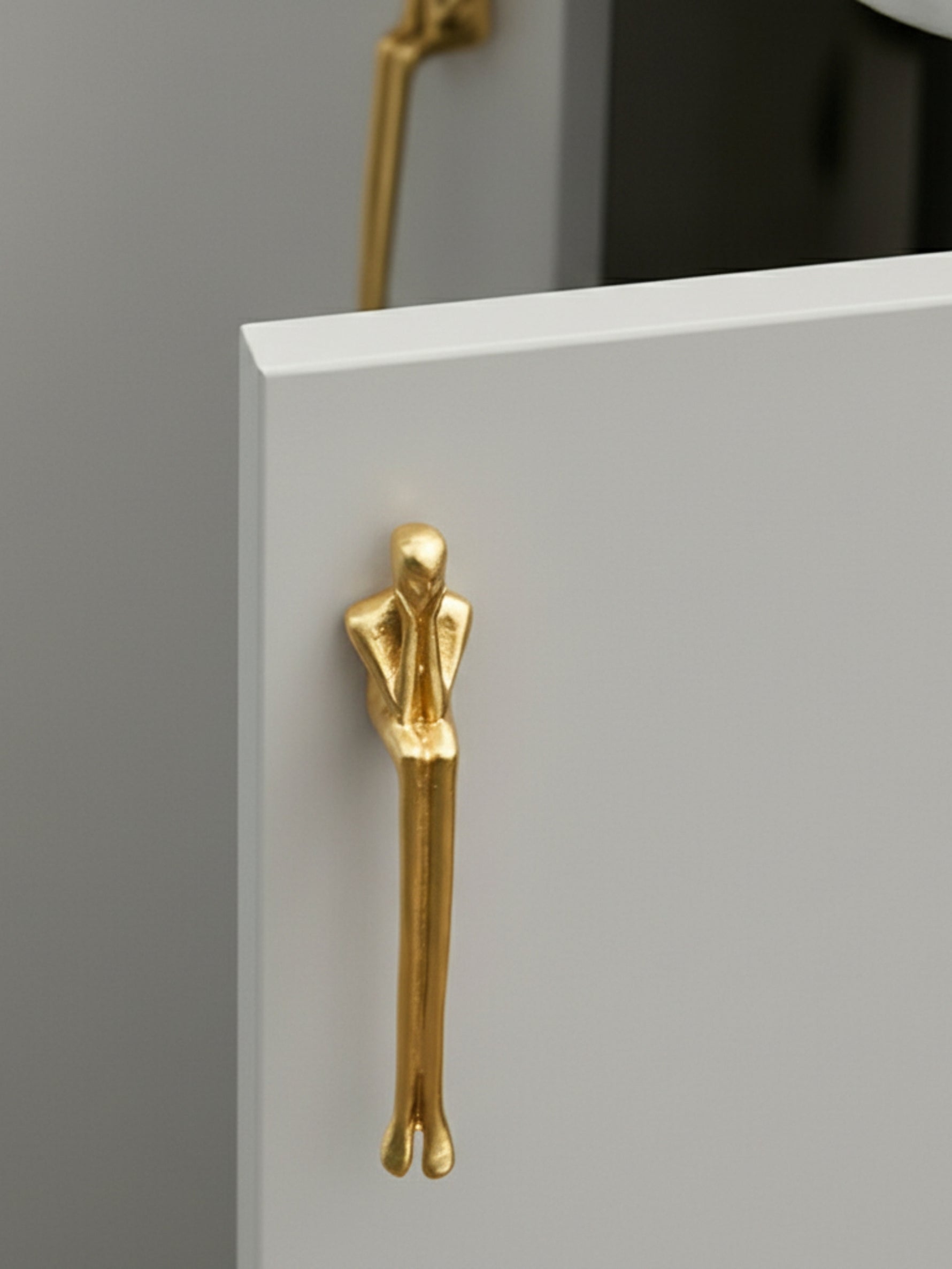 Single gold thinker figure pull on grey cabinet corner