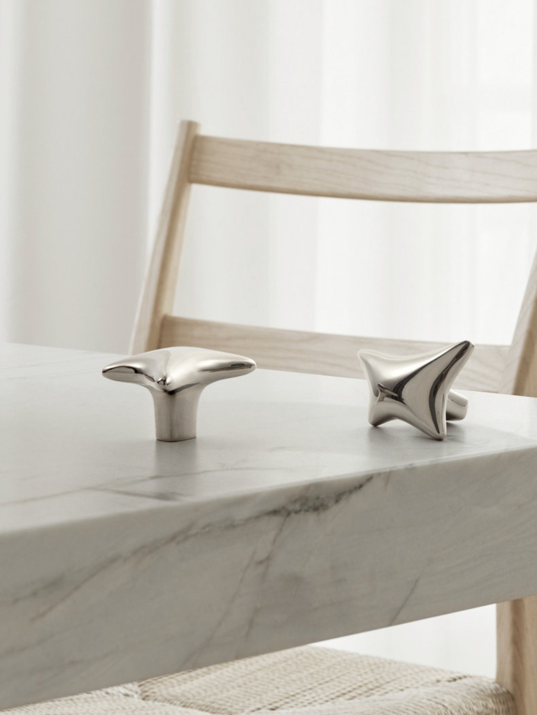 Polished chrome wave star knobs displayed on marble table edge beside wooden dining chair