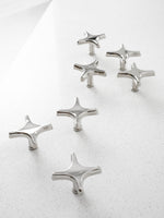 Six polished chrome star knobs and star cross pulls scattered on white speckled countertop