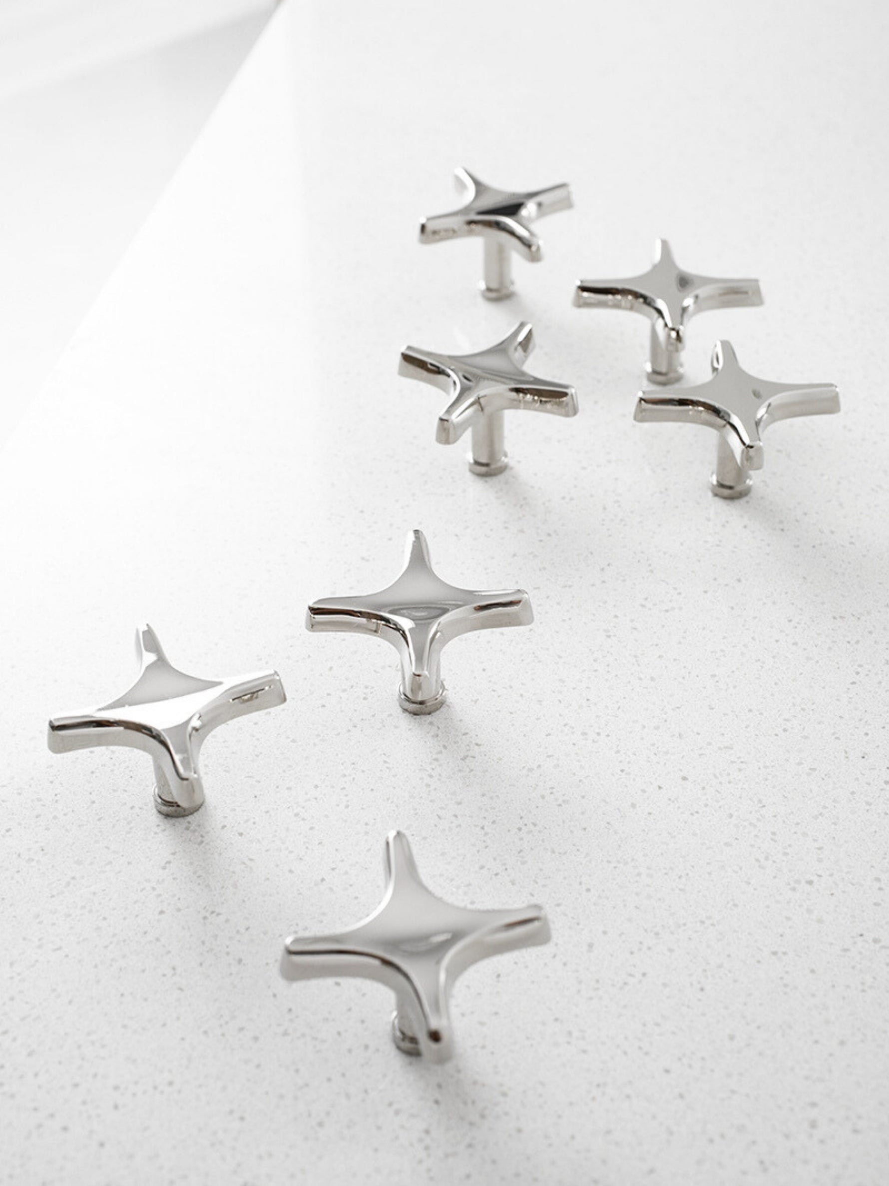 Six polished chrome star knobs and star cross pulls scattered on white speckled countertop