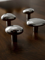 Four polished chrome pebble knobs of varying sizes on dark wood surface