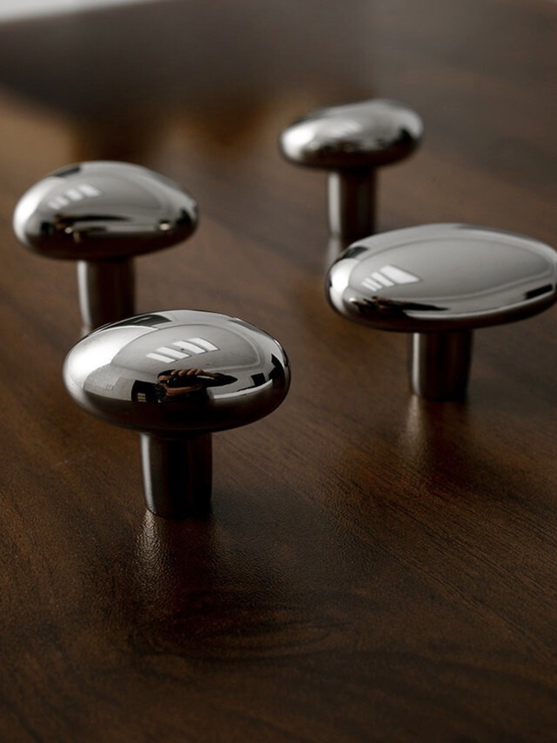 Four polished chrome pebble knobs of varying sizes on dark wood surface