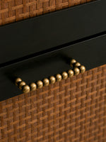 Close-up of a black drawer with a woven brown top and antique brass bead handle.