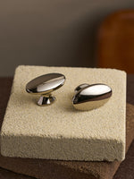 Two nickel silver oval cabinet knobs displayed on textured stone block