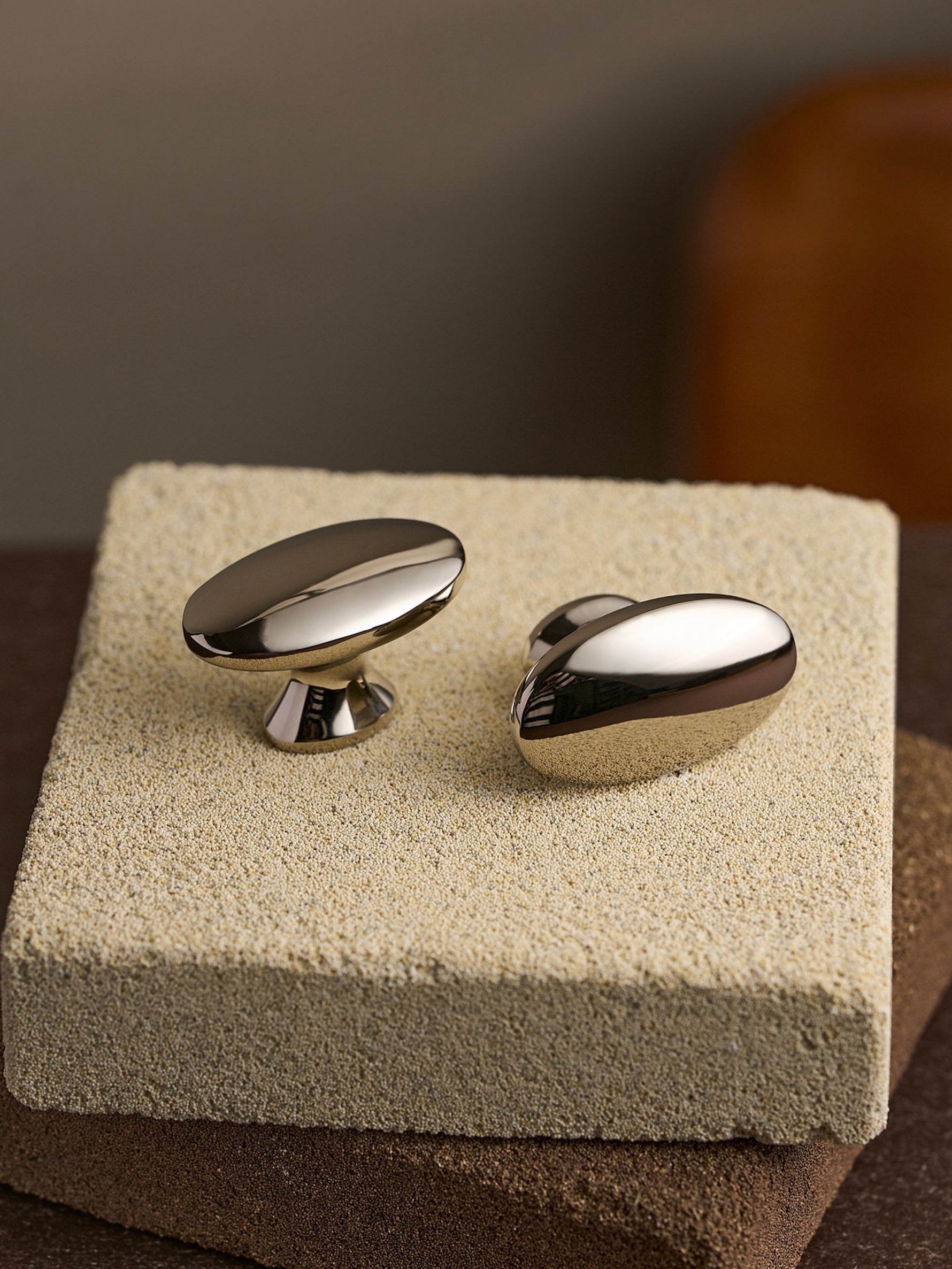 Two nickel silver oval cabinet knobs displayed on textured stone block