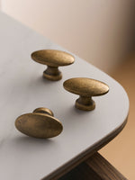 Three antique brass oval knobs on white table with walnut edge, top view