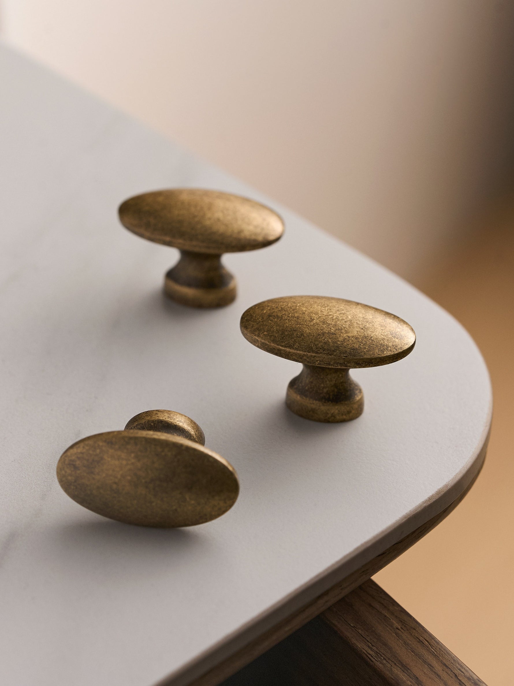 Three antique brass oval knobs on white table with walnut edge, top view