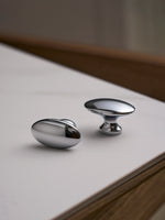 Two polished chrome oval knobs on white surface, different angle
