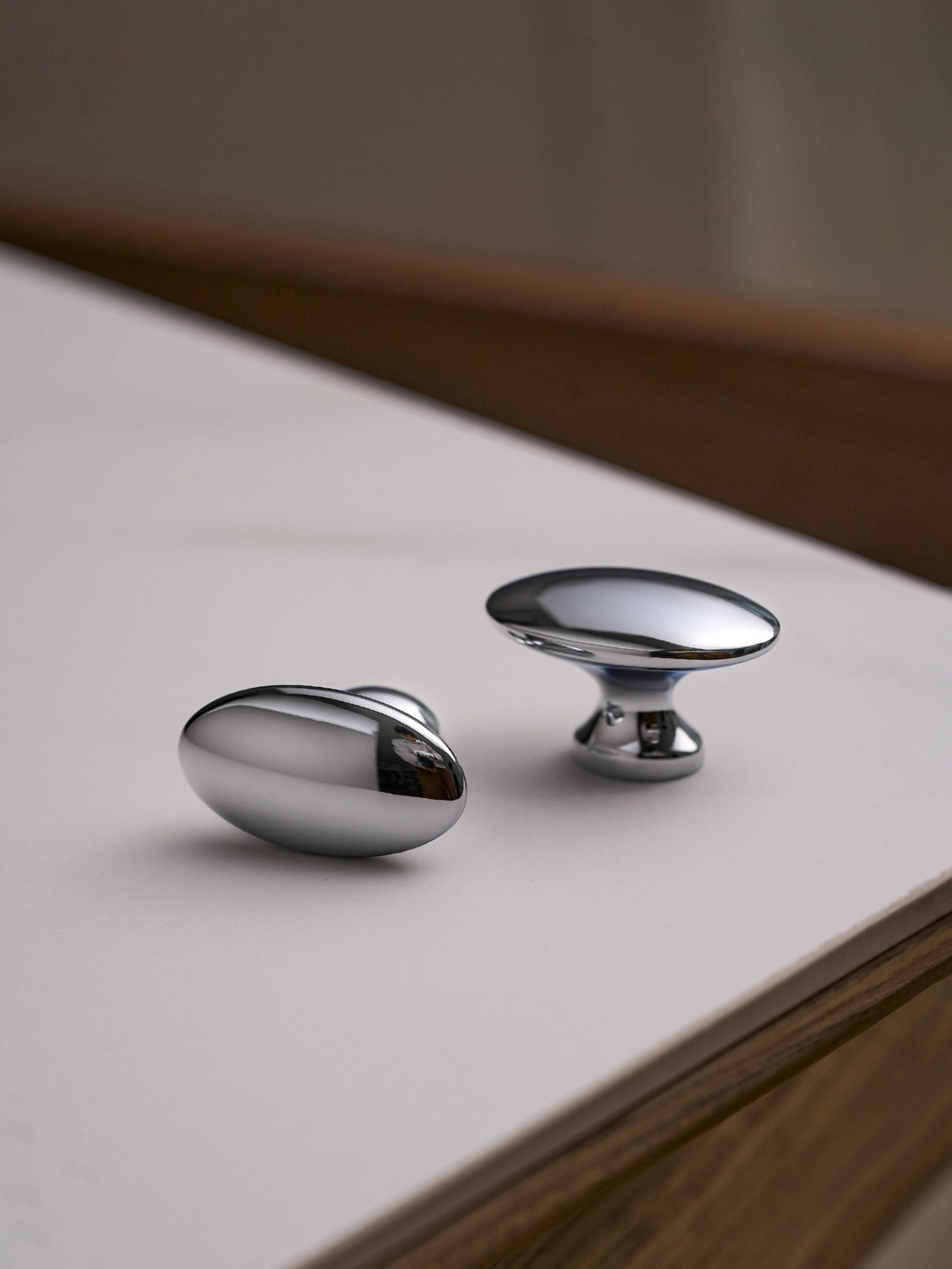 Two polished chrome oval knobs on white surface, different angle