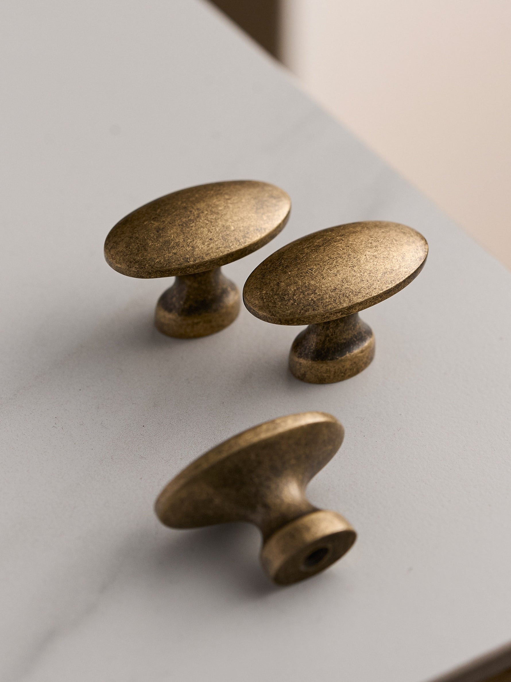 Three antique brass oval knobs on white marble surface
