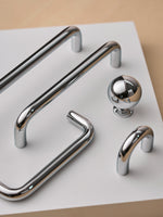 Polished chrome bar pulls, cup pull, and round knob styled on white surface
