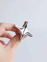 Hand holding a polished chrome star knob showing four-point starburst shape
