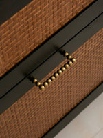 Close-up of a woven drawer with a antique brass handle on a neutral background