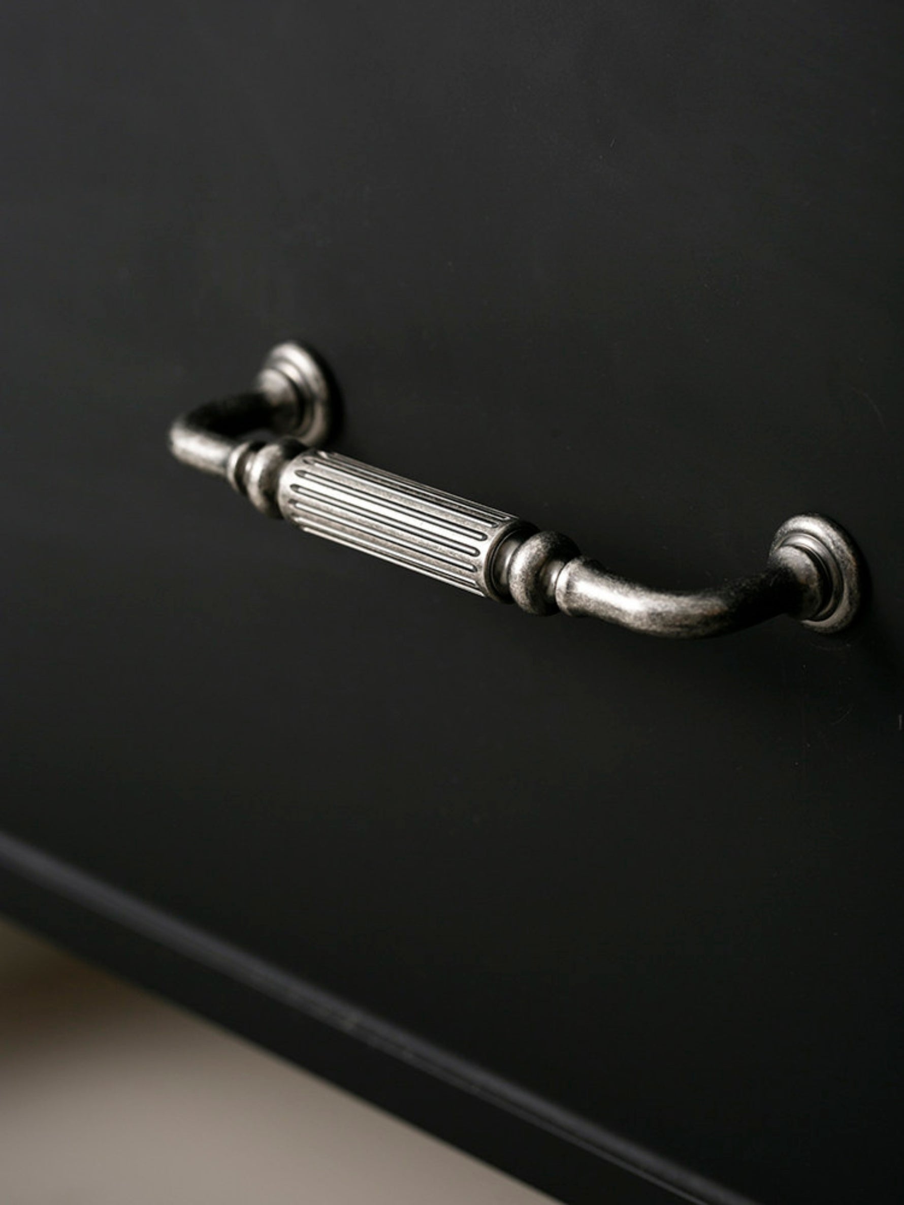 Antique silver reeded cabinet pull on black drawer, close-up side view