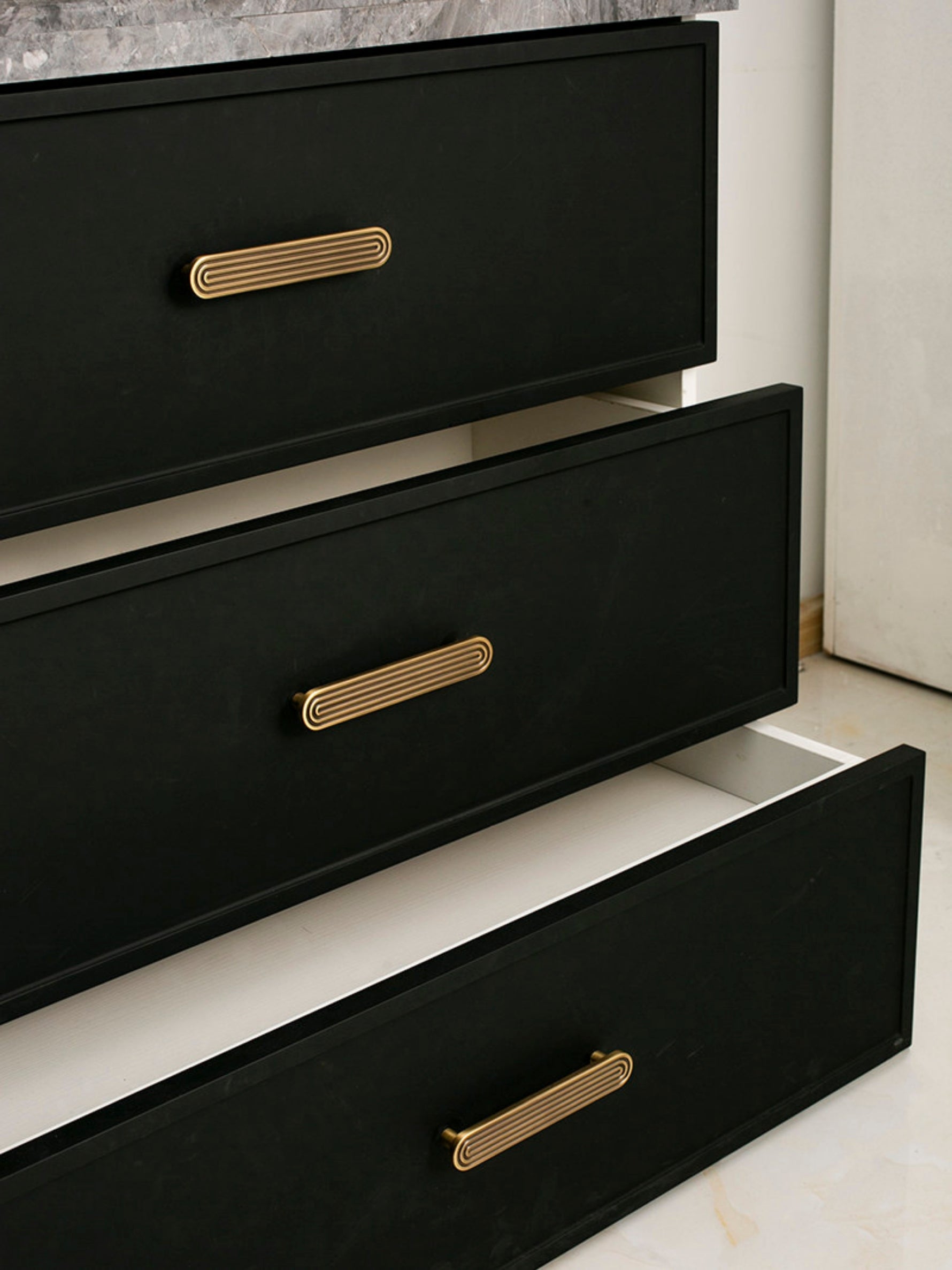 Open black drawer chest showing solid brass Art Deco arch pulls on three drawer fronts