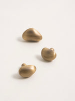 Three brushed brass pebble cabinet knobs flat lay