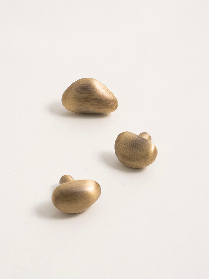Three brushed brass pebble cabinet knobs flat lay