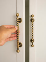 Hand opening a cabinet door with decorative antique brass handles.