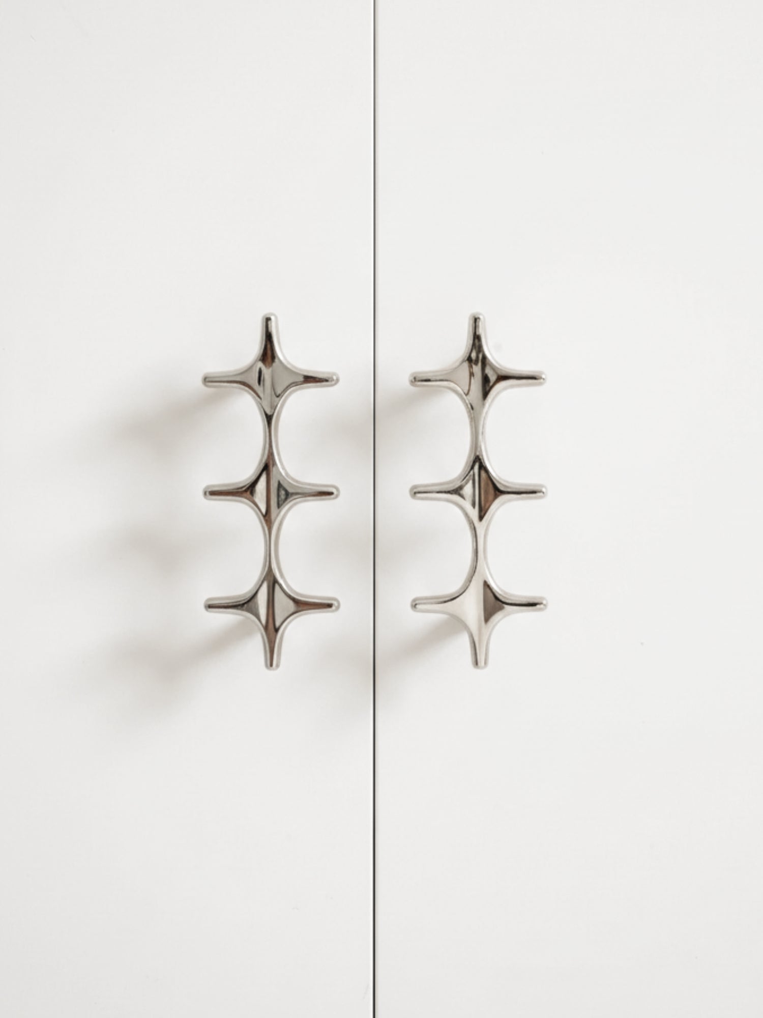 Two polished chrome star cross double pulls on white cabinet doors, front view