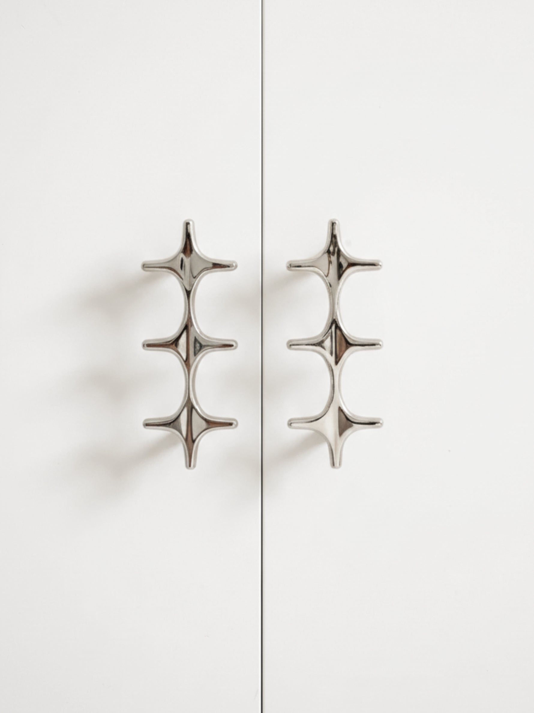 Two polished chrome star cross double pulls on white cabinet doors, front view